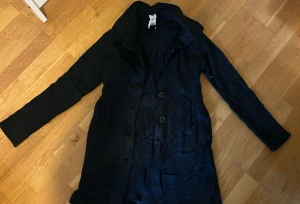 Svart kappa med knappar från Patagonia  - Snygg svart kappa med klassisk krage och stora knappar framtill. Långärmad och med en figurnära passform som ger en stilren siluett. Perfekt för dig som gillar enkel och tidlös design. Materialet känns mjukt och har en matt finish.