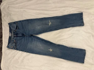 Blå raka jeans från 157 - Snygga blå jeans från 157 med raka ben och slitna detaljer på låren och knäna. Klassisk femficksmodell med orange kontrastsömmar och normal passform. Jeansen är tillverkade i denim och har en tidlös look som passar till det mesta.