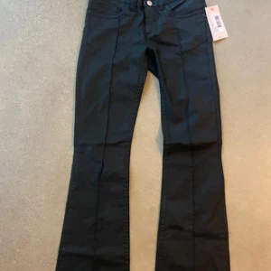 Svarta bootcut byxor med pressveck - Snygga svarta byxor från Nelly med bootcut och markerade pressveck framtill. Byxorna har två knappar i midjan, klassiska fickor och är tillverkade i ett mjukt bomullsmaterial med lite stretch. Perfekt för dig som gillar en stilren och trendig look. Prislappar bifogare, storlek 40 men sitter som 38.