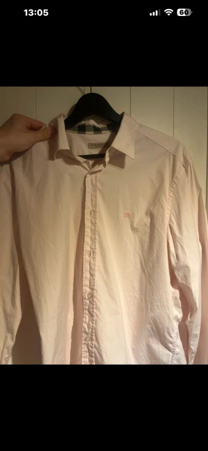 Burberry skjorta - Snygg ljusrosa skjorta från Burberry med klassiskt rutigt mönster på insidan av krage och manschetter. Skjortan har lång ärm, knappar framtill och ett broderat Burberry-emblem på bröstet.  Det står det är en XL men passar bättre som L PRIS DISKUTERBART! 