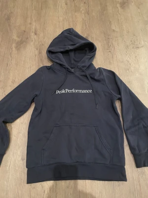 Mörkblå Peak Performance hoodie  - Snygg mörkblå hoodie från Peak Performance i storlek XS. Köpte den nypris för 1200 och den har inte använts mycket då jag växt ur den. Mitt pris är 330 kr. Kom med prisförslag!