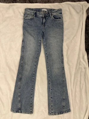 Blå bootcut jeans från Gina Tricot - Snygga ljusblå bootcut jeans från Gina Tricot med klassisk femficksdesign och coola broderade detaljer på bakfickorna. Jeansen har normal passform och är tillverkade i bomull för en skön känsla. Perfekta för dig som gillar retrovibbar och stilren look.
