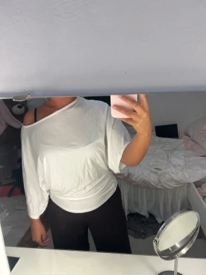 Vit offshoulder topp från Nelly - Säljer en vit offshoulder topp från Nelly i mjuk bomull. Toppen har trekvartsärm och en lös, avslappnad passform som sitter snyggt över ena axeln. Perfekt för dig som gillar en chill och stilren look.