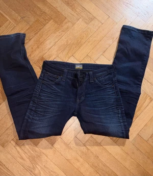 Mörkblå jeans från Lee, straight fit - Snygga mörkblå jeans från Lee med klassisk femficksdesign och raka ben. Jeansen har subtila slitningar framtill och bakfickor med broderad detalj. Passar dig som gillar en tidlös look och vill ha ett par jeans med skön passform. Storlek 164-170