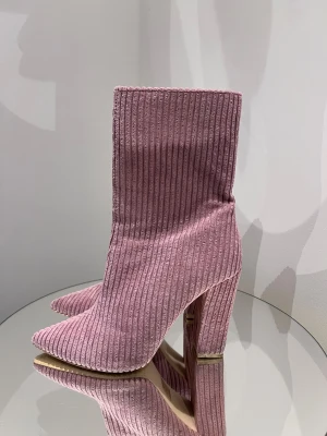 Rosa ribbade stövletter med klack - Säljer ett par snygga rosa stövletter med ribbad struktur och spetsig tå. Skorna har hög klack och är tillverkade i ett mjukt manchestermaterial som ger en cool retrovibe. Perfekt för dig som vill sticka ut med färg och textur på fötterna.