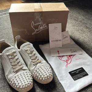Vita Christian Louboutin  - ‼️KVITTO OCH ALLA TAGGAR TILLKOMMER‼️  Snygga vita sneakers från Christian Louboutin i skinn med coola nitar på tån. Storlek 43 men passar även 44. Klassisk rund tå, snörning och platt sula. Kommer med kvitto, originalkartong, dustbag och äkthetskort. Perfekta för dig som vill sticka ut med exklusiv stil. Allt är i bra skick förutom kartongen som är lite sliten. Pris kan diskuteras, skriv gärna vid minsta fundering!
