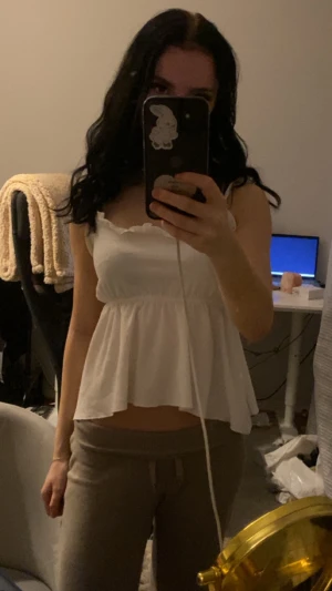 Vit volanglinne - Supersöt vit topp med volangkant upptill och rynk i midjan som ger en flowy och luftig känsla. Toppen är ärmlös och har en lätt strukturerad yta. Perfekt för varma dagar och enkel att styla med jeans eller kjol.