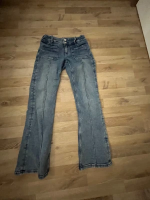 Blå bootcut jeans med framfickor - Snygga blå jeans med bootcut passform och markerade sömmar längs benen. Byxorna har två stora framfickor och två bakfickor samt dubbla knappar i midjan. Perfekta för dig som gillar en retro vibe och vill ha något som sticker ut lite extra.
