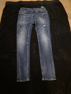  Dondup blå  - Snygga blå jeans med skinny passform och coola slitningar samt små färgstänk på både fram- och baksidan. Klassisk femficksmodell med låg midja och dragkedja. Perfekta för dig som gillar en lite ruffare streetstil.