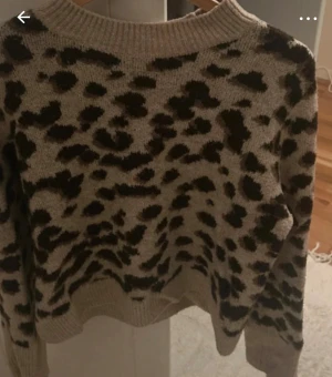 Beige leopardmönstrad stickad tröja H&M - Säljer en beige stickad tröja från H&M i storlek XS med svart leopardmönster. Tröjan har rund hals, ribbade muddar och lång ärm. Perfekt för dig som gillar djurmönster och vill ha en mysig och trendig look.