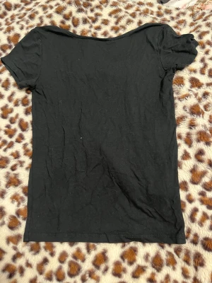 Svart topp med rosett från Lager 157 - Svart kortärmad topp från Lager 157 med en stor, glansig rosett baktill som ger en extra touch. Toppen har rak halsform och är gjord i mjukt bomullsmaterial. Perfekt för dig som gillar stilrena plagg med en twist.