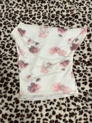 Blommig off shoulder från Gina Tricot - Superfin off shoulder från Gina Tricot i storlek S. Toppen är vit med rosa och lila blommor, har bandeau-form och är tillverkad i mjuk polyester. Perfekt för sommarens alla tillfällen när du vill ha en söt och fräsch look.