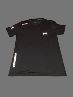Svart Under Armour HeatGear t-shirt - Svart t-shirt från Under Armour med coola reflekterande loggor på bröstet, axeln och längs sidan. Modellen är kortärmad och har en rund hals. Materialet är lätt och andas, perfekt för träning och löpning. Snygg och sportig vibe med fitted passform.