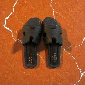 Svarta sandaler Hrmes - Svarta sandaler från Hrmes med ikonisk H-design på ovansidan. Tillverkade i strukturerat skinn med platt sula och öppet tåparti. Märkeslogga i guld på innersulan och Eiffeltornet präglat under sulan. Perfekt för dig som gillar lyxiga detaljer.