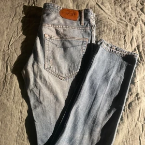 Ljusblå jeans från NN07 - Säljer ett par ljusblå jeans från NN07 med klassisk femficksdesign och slitna detaljer. Jeansen har raka ben och normal passform, tillverkade i bomullsdenim. Snygga kontrastsömmar och läderpatch bak i midjan. Perfekta för en avslappnad stil. Nytt pris: 1700kr. Mitt pris: 500kr. Hör av er vid funderingar!