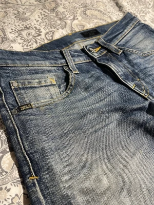 Tiger of Sweden blå jeans slim fit - Snygga blå jeans från Tiger of Sweden med klassisk femficksdesign och gul kontrastsöm. Jeansen har en straight fit och är tillverkade i slitstarkt denim med snygga tvättade detaljer. Perfekt för dig som gillar stilrena och tidlösa jeans.