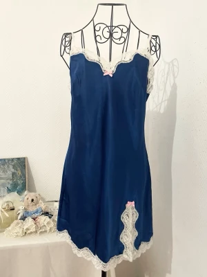 Marinblå nattlinne från Victoria's Secret - Supersöt marinblå kort satinklänning från Victoria's Secret med vit spetskant och två ljusrosa rosetter. Storlek: M, passar strl. 36-38. Dockan är i storlek 34.