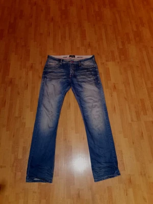 Blå jeans från Hampton Republic 34/34 - Säljer ett par blå jeans från Hampton Republic med klassisk femficksdesign och snygga slitningar. Jeansen har normal passform, raka ben och är tillverkade i 100% bomull. Märkesdetaljer på bakfickan och midjebandet ger extra stilpoäng. 