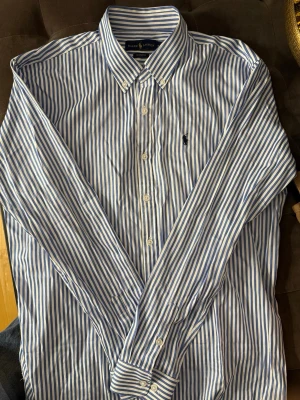 Ralph Lauren Skjorta - Blå vit randig Ralph Lauren skjorta i toppenskick, strl M. Använd ett fåtal gånger och inga tecken på användning. Kom med prisförslag om priset inte passar.