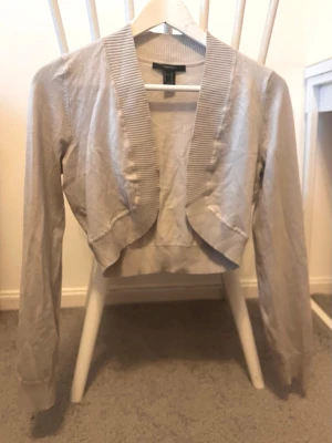 Beige kofta - Snygg beige kofta med ribbad krage och muddar. Modellen är croppad och har långärmade ärmar. Perfekt att slänga över en topp för en chill look. Materialet är mjukt och känns som bomull.