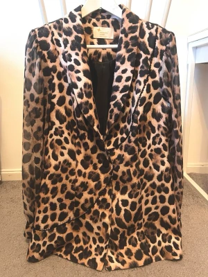 Leopardmönstrad kavaj - Snygg kavaj med leopardmönster. Jackan har klassisk krage, knappar framtill och är långärmad. Materialet är lätt och känns skönt mot huden, perfekt för att sticka ut med en cool look. Passformen är normal och färgerna går i beige och svart.