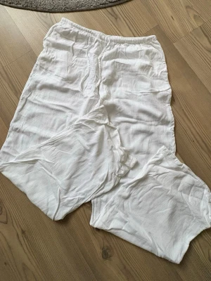 Vita linnebyxor med snörning - Säljer ett par vita linnebyxor med elastisk midja och snörning framtill. Byxorna har rak passform och är tillverkade i ett lätt och luftigt linnematerial, perfekt för varma dagar. Stilrena och enkla att matcha med olika toppar.
