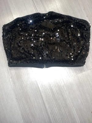 Svart paljett-tubtopp från SHEIN - Glittrig svart tubtopp från SHEIN täckt med svarta paljetter, de ser blått ut pga blixt🙏🏻💕