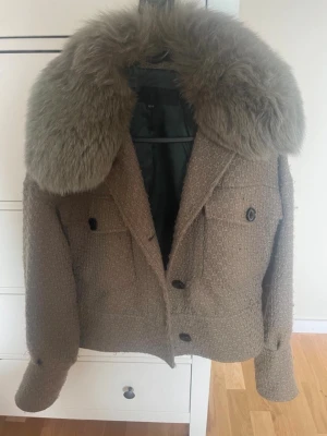 Brun pälsjacka med stora knappar - Säljer en brun/grön pälsjacka med stor fluffig krage i fuskpäls. Jackan har en croppad passform, stora svarta knappar framtill och två fickor med lock. Materialet är grovt vävt och ger en lyxig känsla. Perfekt för dig som vill sticka ut med en unik och trendig jacka. Fluffet på jackan drar åt de gröna hållet!💚🥰 DEN ÄR AVNOPPRAD EFTER DESSA BILDER ÄR TAGNA