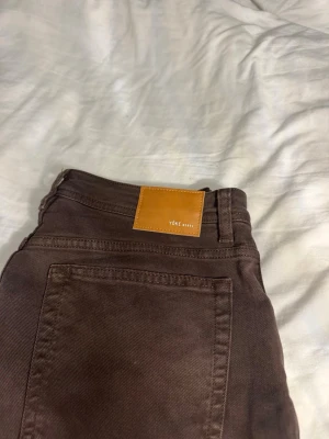 Bruna raka jeans från Yoke, M - Säljer ett par bruna jeans från Yoke i storlek M. De har klassisk femficksdesign, rak passform och dragkedja i gylfen. Materialet är slitstark bomull och färgen är mörkbrun. Perfekt för dig som gillar stilrena och enkla jeans.