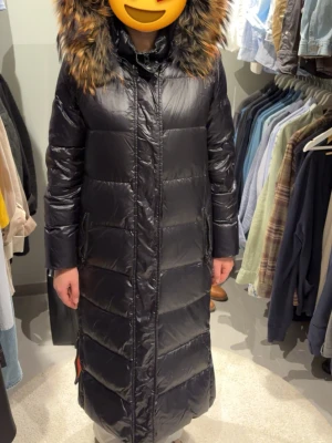 Svart lång dunjacka Rockandblue - Säljer en original RockandBlue lång dunjacka i svart med äkta pälskrage. Jackan är varm, stilren och i fint skick överlag. OBS!  Dragkedjan på vänster sida kan ibland fastna när den dras upp hela vägen, vilket gör att den kan vara lite trög att dra ner. I övrigt fungerar dragkedjan och jackan utan problem.