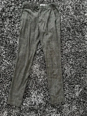 Chinos från Jack & Jones - Här är ett par riktigt snygga byxor från Jack & Jones Pants Studio för dig som vill ha något lite mer unikt än bara enfärgat. Byxorna har en Slim fit som ger en modern och skarp passform. De fungerar precis lika bra på kontoret med en skjorta som till en enkel hoodie när du vill uppgradera din vardagsstil. • Storlek: 28 i midjan och 32 i längd. • Nypris:1100kr