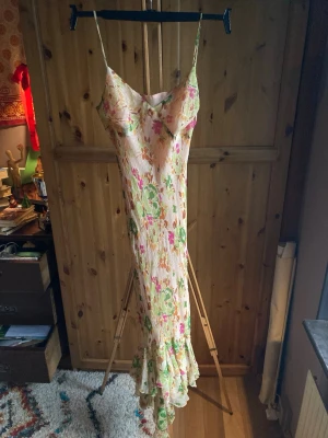 Balklänning med tropisk känsla - Gjort i ett tunnt lite genomskinligt material med dubbla lager, det innersta är lent och sitter lätt mot kroppen och det yttersta har mönster med små gulddetaljer och rosa och gröna blommor. Har en stor byst och tunna band där ett utav banden är lite slitet. Köpt på secondhand men utöver bandet är den i mycket bra skick