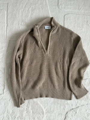Beige stickad tröja med half zip från Grunt - Säljer en beige stickad tröja från Grunt i storlek S. Tröjan har en ribbad struktur, hög krage och en snygg half zip-dragkedja framtill. Perfekt för lager-på-lager och chill stil under höst och vinter. Passformen är normal och ärmarna är långa.