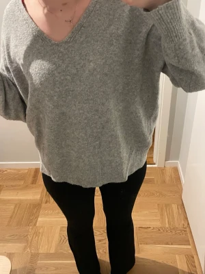 Grå stickad tröja Pull&Bear S - Mysig grå stickad tröja från Pull&Bear i storlek S. Tröjan har v-ringad hals, ribbade muddar och en loose passform. Perfekt för lager-på-lager och chill dagar. Materialet är mjukt och värmande, och den har långa ärmar med breda muddar.