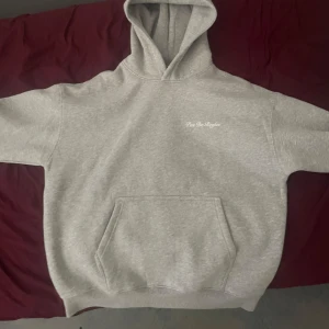 Grå hoodie No Rules Pas De Regles - Säljer en grå hoodie från Pas De Regles med vit text på bröstet och stor print på ryggen: 'No Rules, It's a lifestyle'. Tröjan har huva, magficka och ribbade muddar. Perfekt för chill dagar och streetwear-vibe.