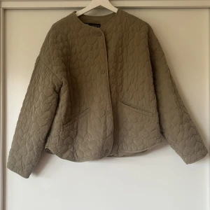 Quiltad beige jacka från Zara, M - Superfin quiltad jacka från Zara i grön med hjärtformat mönster. Jackan har rund halsringning, tryckknappar framtill och två fickor. Oversized passform och långa ärmar, perfekt för lager-på-lager. Materialet är mjukt och känns riktigt skönt.