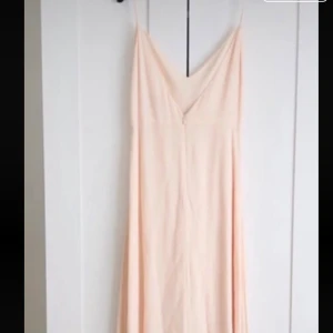 Champagnefärgad långklänning - Elegant långklänning i champagnefärg med smala axelband och v-ringning. Klänningen har en flowy siluett och är tillverkad i ett lätt, mjukt material som ger ett luftigt intryck. Perfekt för sommarens alla tillfällen. Köptes för 1000 kr. Har används kan ha någon fläck men väldigt vacker. Har ett par vackra klackskor som passar till de. Märket Zetterberg!