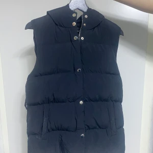 Ny Svart väst (priset kan diskuteras vid snabb affär) - Svart väst med, mysig huva och tryckknappar framtill. Västen har en quiltad design och två fickor på sidorna. Perfekt för lager-på-lager och chill höst- eller vinterstil. Priset kan diskuteras vid snabb affär!