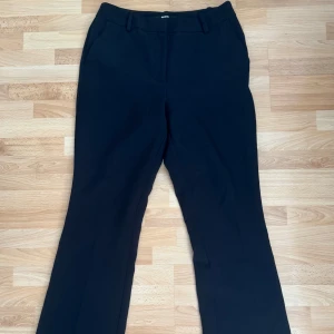 Svarta kostymbyxor från BikBok, stl 38 - Svarta kostymbyxor från BikBok i storlek 38. Byxorna har klassisk rak passform med hällor för bälte och sidfickor. Tillverkade i ett stretchigt material av 93% återvunnen polyester och 7% elastan för extra komfort. Använd få gånger.