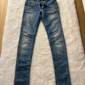 Blå low waist skinny jeans från G-Star Raw - Snygga blå low skinny jeans från G-Star Raw med klassisk femficksdesign och dragkedjor på bakfickorna. Jeansen har en lätt tvättad look och smal passform som sitter tajt längs benen. Perfekta för dig som gillar en modern och stilren vibe.