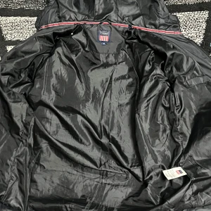 Svart dunjacka från Morris, M - Svart dunjacka från Morris med huva och quiltad design. Jackan har dragkedja framtill, diskret logomärke på ärmen och är tillverkad i glansig polyester. Perfekt för kyliga dagar och har en clean, modern look.