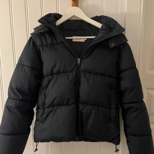 Populär marinblå pufferjacka från Nelly! - Förra årets populära jacka från Nelly! Säljer en svart pufferjacka från Nelly med huva och dragkedja framtill. Jackan är vadderad, har långa ärmar och praktiska fickor med knappstängning. Perfekt för kalla dagar och har en snygg, lite boxig passform. eftersom den it säljs längre och inte är så sliten , det påverkar priset! Men priset går såklart att diskutera