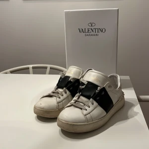 Valentino Garavani Open sneakers vit/svart - Säljer ett par Valentino Garavani Open. Skick 7/10 - Har ett hål under sulan, hålet går inte igenom sulan.( Se på bild 4) annars Inga defekter. Pris 1399kr, kan absolut sänka vid snabb affär, Byten kan tänkas också, det är bara att höra av er, samt vid frågor eller funderingar.