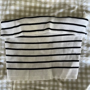 Randig ribbad tubtopp från New Yorker  - Säljer en vit och svart ribbad tubtopp från New Yorker. Toppen är bandeau-modell, har horisontella svarta ränder och är stickad i ett stretchigt material. Perfekt för dig som gillar en enkel men snygg look. 