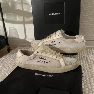  Saint Laurent skor strl 45 - Säljer ett par vita sneakers från Saint Laurent i bra skick strl 45 men sitter mer som 44. Riktigt snygga och passar till nästan allt. Låda, dustbag och kort medföljer. Priset är INTE hugget i sten!(litet hål som är lappat på högra skon men de är bara en liten defekt)(också ett litet hål på vänstra skon på samma ställe, som inte är lappat.) innersulorna är även slitna.