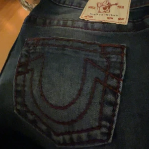 True Religion blå jeans med röd söm - Säljer ett par blå jeans från True Religion med röda söm på bakfickan. Har använts 2 gånger, köpte en storlek för stor. Ordinarie pris om man köper dom nya är 1400kr