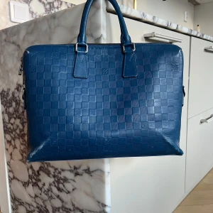 Louis Vuitton Porte Documents Damier  - Säljer en blå datorväska från Louis Vuitton i skinn med klassiskt rutigt mönster. Perfekt för dig som vill ha en snygg och stilren väska till plugget eller jobbet. Äkta väska, köpt för ca 1 år sedan hos Aretrotale. Bredd:37cm Höjd: 26,5cm Djup:6cm
