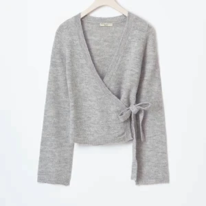 Grå omlottkofta med knyt - Supermjuk grå omlottkofta från Twist & Tango med v-ringning och knyt i sidan. Långärmad och ribbad vid muddar och nederkant. Perfekt att slänga på sig för en chill look, funkar lika bra till jeans som till kjol. Endast använd ett fåtal gånger och tröjan e slutsåld på hemsidan!