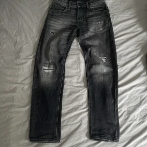 Mörkgrå jeans från jack&jones med slitningar - Snygga mörkgrå jeans från Jack & Jones, modell Tapered/Mike i storlek W28/L32. Jeansen har slitna detaljer och är regular fit!Nästan oanvända och inga defekter på jeansen😮‍💨Dm för mera info!👑
