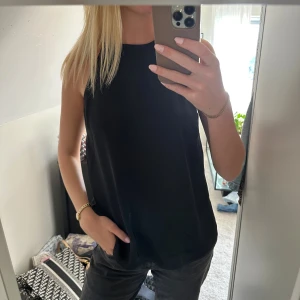 Svart ärmlös linnetopp från H&M - Säljer en svart, stilren linnetopp från H&M i storlek S. Toppen har hög halsringning, smala axelband och är helt ärmlös. Materialet är mjukt och har en lätt glansig finish som ger en snygg look. Perfekt att matcha med jeans eller kjol för en clean stil.